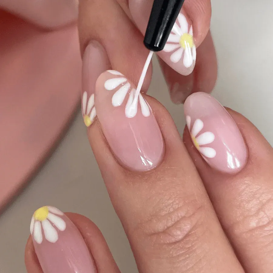 Handmålad blommig nageldesign med prästkragar på ljusrosa naglar.